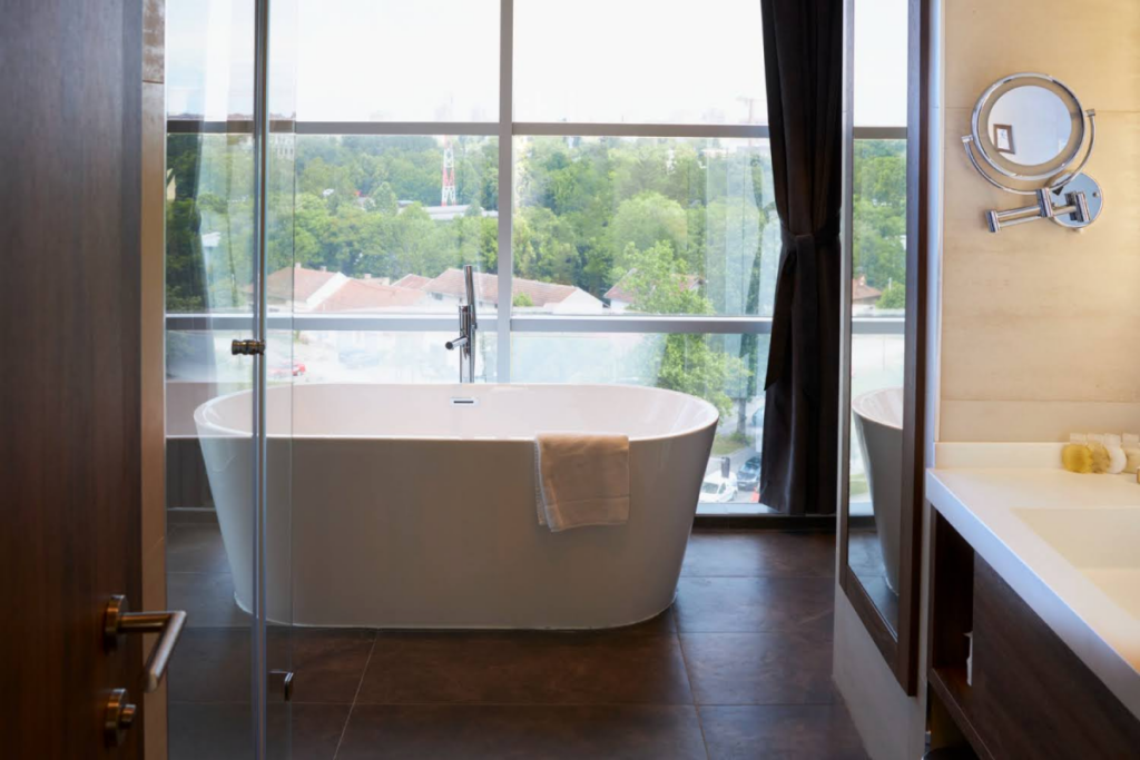 A bathroom with a freestanding tub and large window, showcasing spa-like, natural light-filled designs.