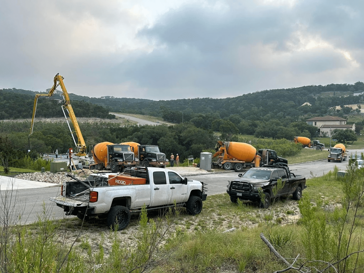 Several cement trucks parked on a construction site with a view of rolling hills in the background.