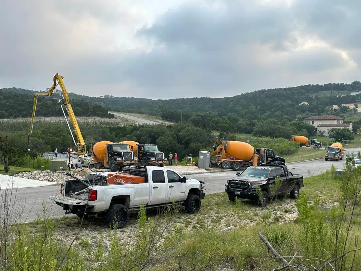 Several cement trucks parked on a construction site with a view of rolling hills in the background.