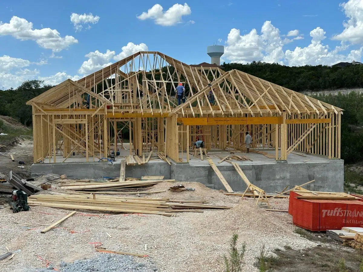 A house under construction with wooden framing and workers on the roof.