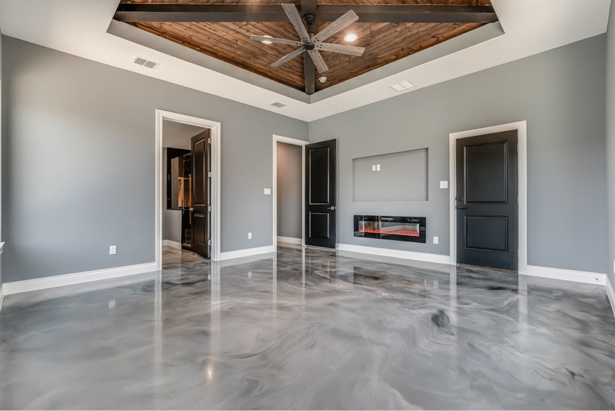 A spacious room with a gray metallic floor, a wood-beamed ceiling, and a fireplace.