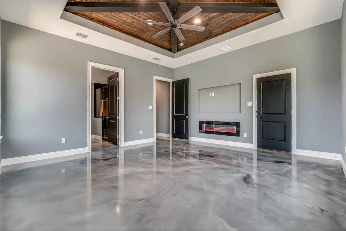 A spacious room with a gray metallic floor, a wood-beamed ceiling, and a fireplace.