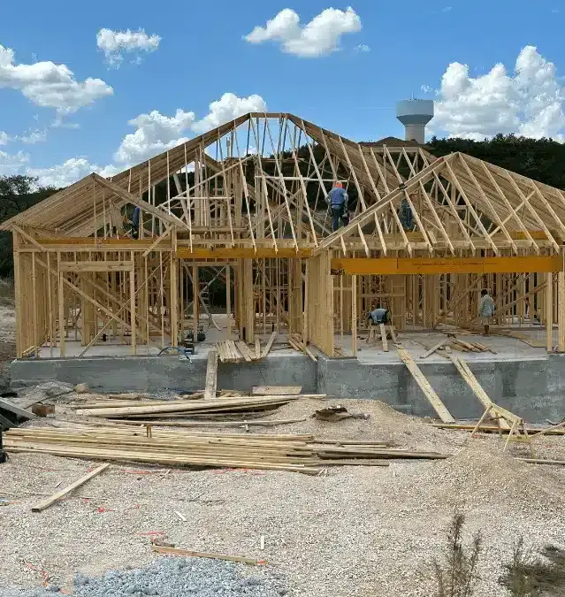 A house under construction with wooden framing and workers on the roof.