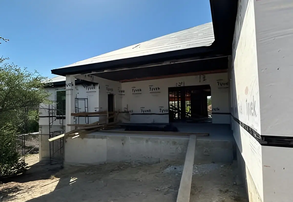 A house under construction with wooden framing and workers assembling the roof structure.