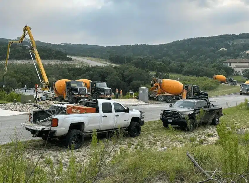 Several cement trucks parked on a construction site with a view of rolling hills in the background.