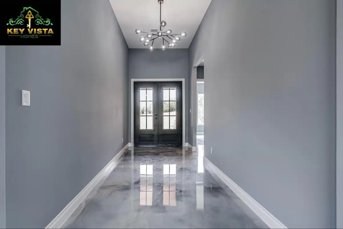 A stylish entryway painted in gray, featuring a modern chandelier, double doors with glass panels, and a reflective gray epoxy floor.