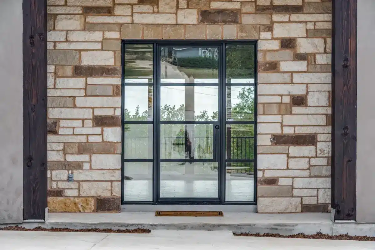 Close-up of a black-framed glass door set in a stone facade, offering a stylish, modern entrance to the home.