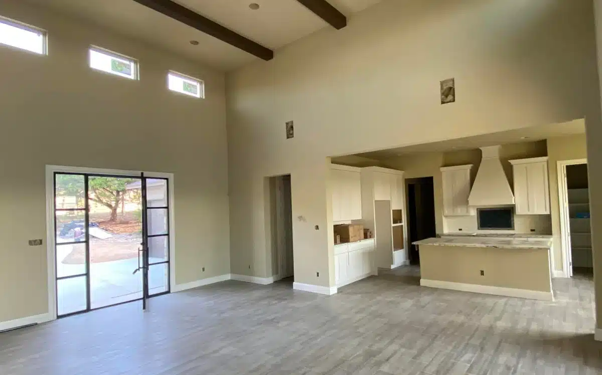 Bright, open living room featuring a vaulted ceiling with wooden beams, light neutral walls, tall windows near the ceiling.