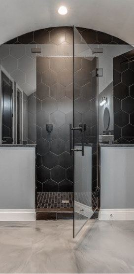 Modern Home Builder in Boerne, TX 7 A modern bathroom with a large glass shower enclosure, black hexagonal tiles, and a metallic floor.